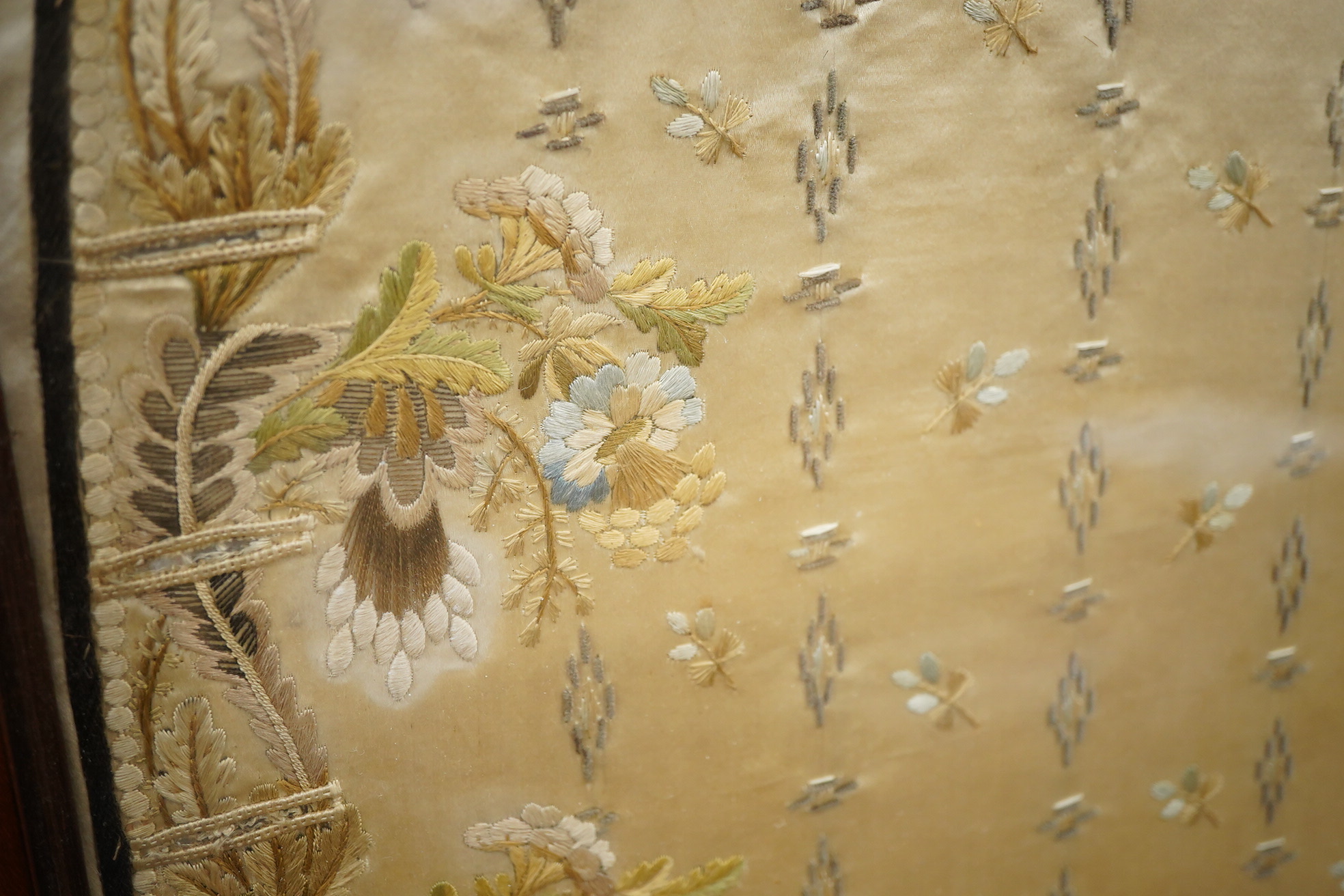 A framed front panel of a Regency silk embroidered waistcoat, ornately worked in fine polychrome silks with vining stems of leaves and hanging flowers framing a small spot motif interior, 60cm x 59cm. Condition - the sil